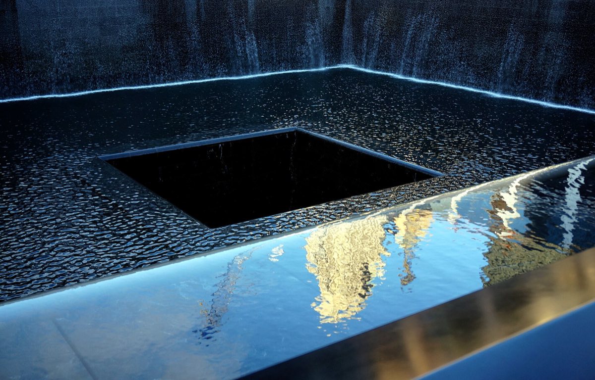 A reflecting pool at the National September 11 Memorial, with water falling into the square void and names inscribed on the bronze parapet